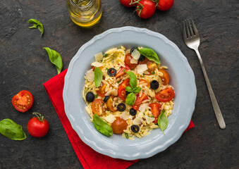 Salad with orzo pasta, tomatoes, olives and parmesan in a gray plate on a black concrete background. Pasta salad recipes.