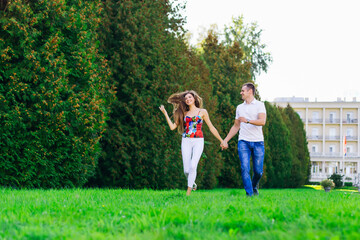 Obraz premium cheerful couple, holding hands, runs on green grass in nature. The woman waves her hair.