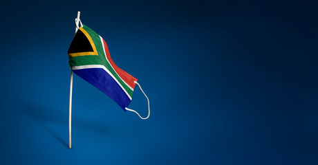 South Africa mask on dark blue background. Waving flag of South Africa painted on medical mask on pole. Concept of The banner of the fight against the epidemic coronavirus COVID-19. Copy space