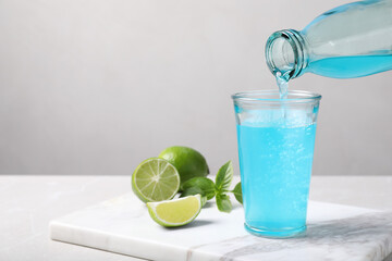 Pouring refreshing light blue drink into glass on white table, space for text