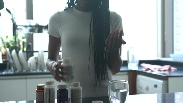 Black woman with braided hair taking her vitamins and supplements in the kitchen 