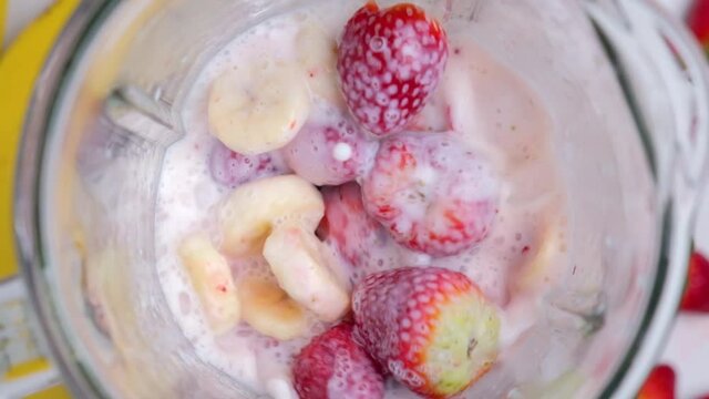 Cooking strawberry and banana milkshake in blender with splashes. top view. slow motion. Healthy drink concept