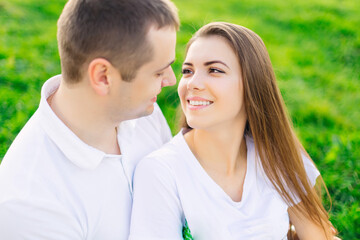 A young couple looks at each other and smiles while sitting on a blanket in a park in nature.