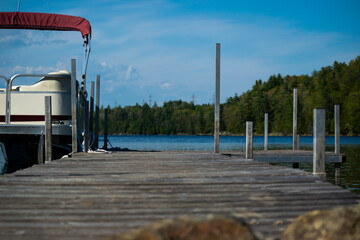 Pontoon boat on aqua blue lake.  Old brown woooden dock floating in water with water vehicle.  wood structure.