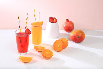 Modern still life with citrus, orange juice and oranges, pomegranate, strawberry and mango on stand and podiums on pink background with long hard shadows, 

