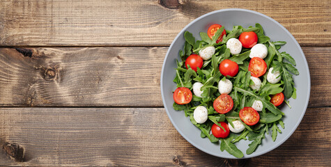 Diet and healthy salad with arugula, cherry tomatoes, mozzarella cheese on table wooden background. Mediterranean food. Top view, flat lay, banner, copy space