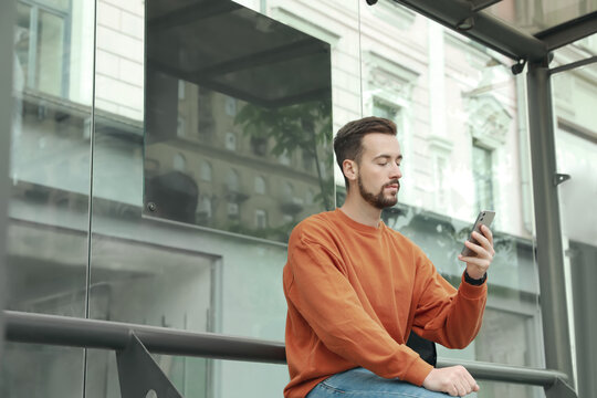 Young man with smartphone waiting for public transport at bus stop