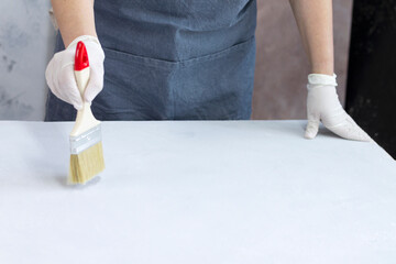 A girl artist using a brush and white paint primed the surface of a plywood sheet with a copy of...
