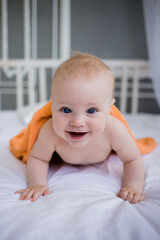 a happy little boy lies in an orange towel on the bed in the bedroom and looks at the camera. Vertical orientation