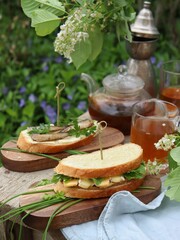 Picnic in the garden. In the garden there is an old wooden table for tea drinking. On the table, various sandwiches with cheese and greens, with butter and fish, a teapot with green tea, cups. Summer