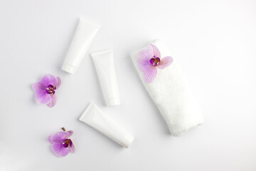 Cosmetic mock-up. White tubes with cream or lotion and a white towel next to it. Treatment in the...