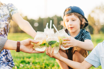 Family with two children summer picnic in nature. Little boys hold yellow and green glasses with cold lemonade in their hands. Kids drinking a refreshing drink from the straw. Selective focus. - obrazy, fototapety, plakaty