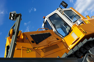 Bulldozer, huge yellow powerful construction machine with grey tracks, heavy industry, bottom view, white clouds and blue sky on background