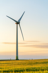 Green field at sunset on a summer day with scattered clouds with a wind turbine in a windfarm where...