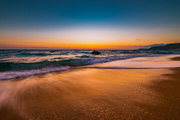 Ocean water flowing over rocks and beach with golden sunrise