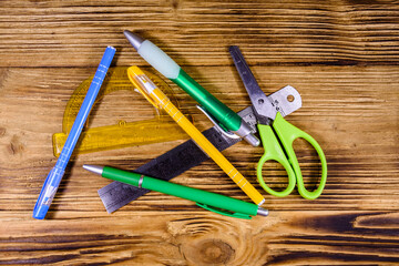 Multi colored ball pens, protractor, scissors and ruler on a wooden table. Top view