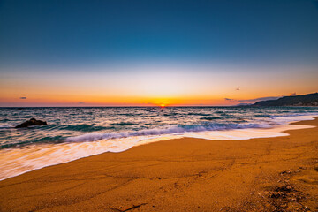 Ocean water flowing over rocks and beach with golden sunrise