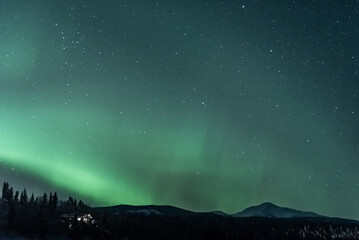 Mountain view landscape in northern Canada with aurora borealis seen northern lights dancing in green sky. 