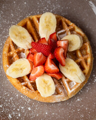 Waffle on a plate with strawberry, banana, and confectioner's sugar.