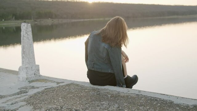 A girs in the sunset, in a black dress , the wind blows her hair .