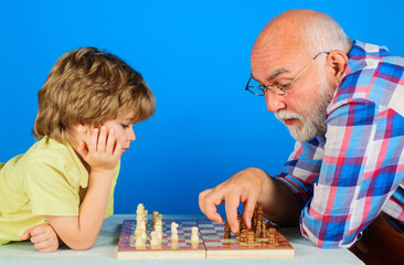 Grandson playing chess with grandpa. Grandfather teaching grandchild play chess. Family relationship.