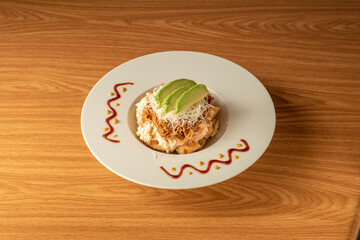 Arepa on a plate with shredded meat, grated cheese, avocado and mayonnaise sauce