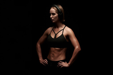 Obraz premium Young female with muscular body getting ready to workout and listen music in headphones