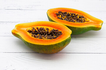 Half of ripe papaya fruit with seeds on white wooden table background.