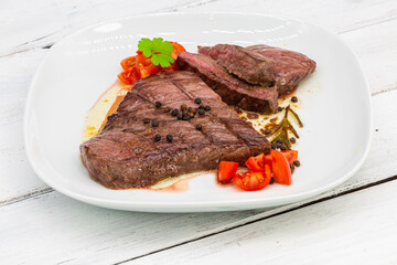 Fresh grilled beef meat. Steaks and spices on white dish isolated on white wooden table