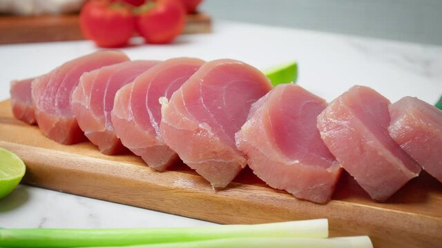 Closeup of Sliced Raw Tuna Yellowfin on a table with greens and vegetables in 4K. Healthy meat, fresh tuna cut in pieces on a chopping board.