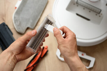 A man cleans the hepa filter from a robot vacuum cleaner with a special brush