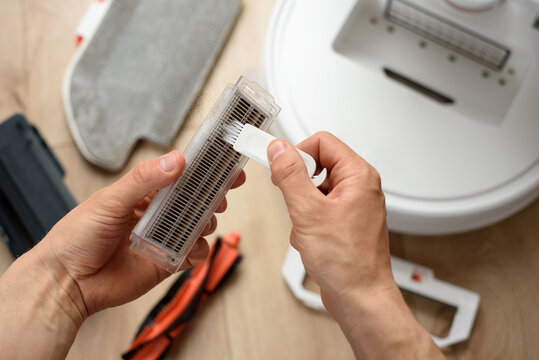 A Man Cleans The Hepa Filter From A Robot Vacuum Cleaner With A Special Brush