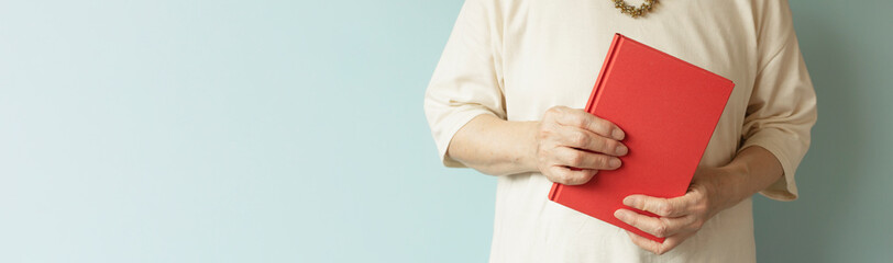 My book. Elderly woman holding a red book.　私の本。赤い本を持つ高齢の女性。