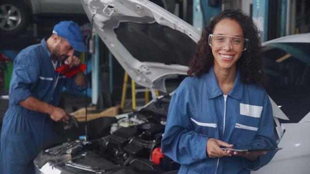 Team of mechanic with man in uniform fix and repair engine car and woman holding tablet computer smiling for examining in the garage, auto service, technician with diagnostic and checking vehicle.