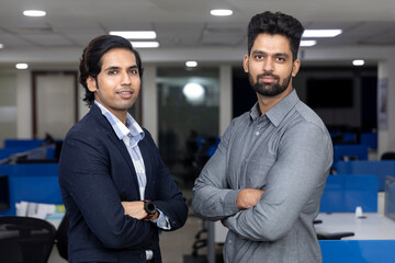 Portrait of two young handsome Indian businessmen standing against office background, corporate...