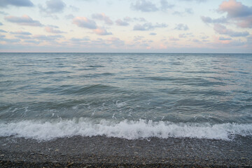 The sunrise over the calm sea casts rays of orange light into the air as the setting sun penetrates through the clouds into the picturesque calm seascape