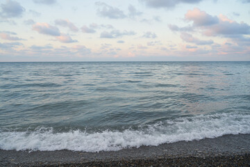 The sunrise over the calm sea casts rays of orange light into the air as the setting sun penetrates through the clouds into the picturesque calm seascape