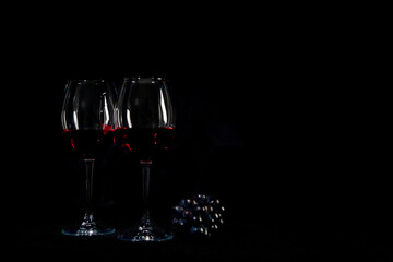 Red wine bottle with 2 glasses and bottle opener on black background.