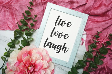 Live Love Laught written on blue frame with pink flower flat lay on marble background