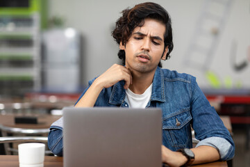 Portrait of a young handsome Indian man working on his laptop, sitting in an office cafeteria, coffee shop, casual work environment.