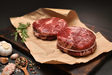 Fresh raw pieces of beef meat with ingredients for cooking on a wrapping paper in kitchen
