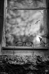 Vintage reading glasses lie on window sill against the window reflection of clouds - Black and White