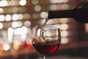 Pouring rose wine from bottle into glass on blurred background, closeup