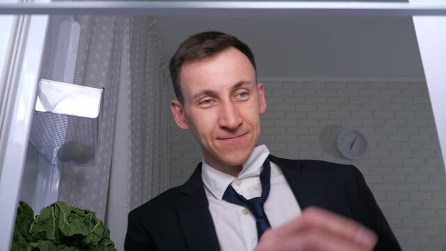 Happy Man In Office Suit And Tie Looks For To Take Bottle Of Cold Beer From Shelf In Dark Kitchen, Close View From Inside New Refrigerator