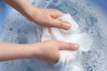 Top view of woman hand washing white clothing in suds, closeup - obrazy, fototapety, plakaty