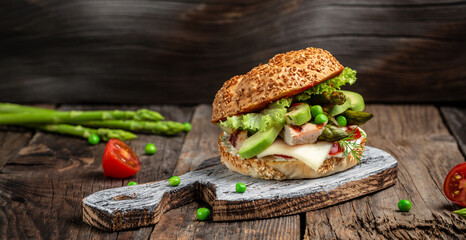 Tasty grilled homemade burgers with chicken fillet, asparagus, avocado, tomatoes, peas, cheese and tartar sauce on rustic wooden background. fast food and junk food concept