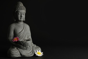 Beautiful stone Buddha sculpture with flowers on black background. Space for text