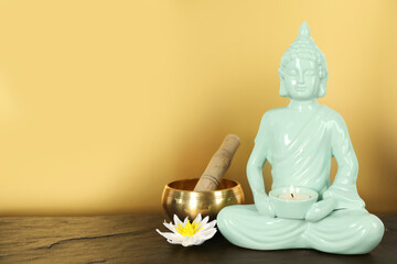 Buddha statue with burning candle near lotus flower and singing bowl on black table. Space for text