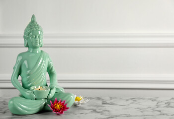 Buddha statue with burning candle and lotus flowers on white marble table. Space for text
