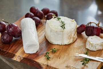 Selected French cheeses with grapes, on wooden board with rosemary and knife